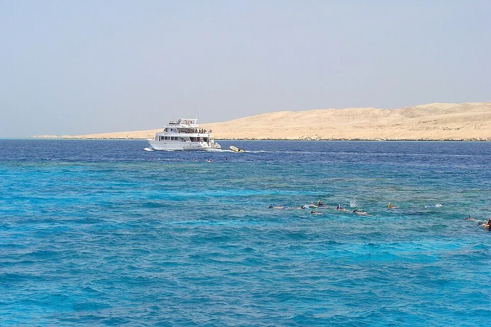 Mahmya Island beach with shaded pergolas, wooden walkways, and calm turquoise water lapping gently at the sand.