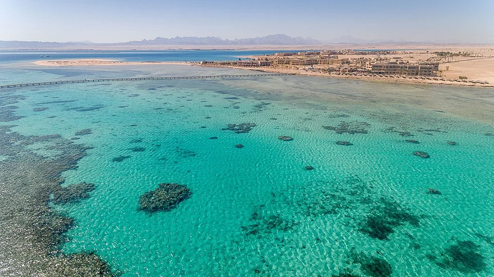 Aerial view of Soma Bay’s sandy peninsula extending into the Red Sea with shallow turquoise water and darker blue drop-offs beyond the reef.