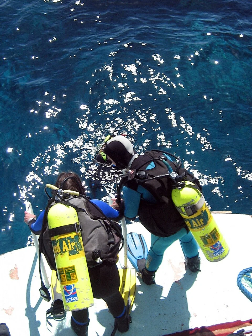 Divers gear up on the stern platform of a white day boat in Hurghada, with crew assisting and tanks neatly racked.