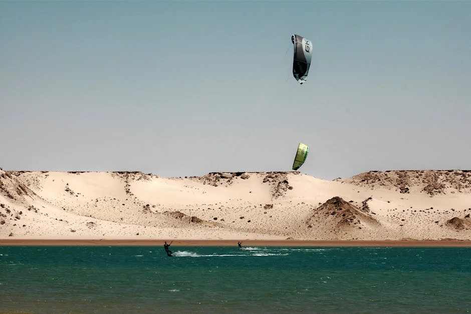 A kitesurfer rides across Dahab’s turquoise lagoon with whitecaps indicating steady summer wind at about 18 to 22 knots.