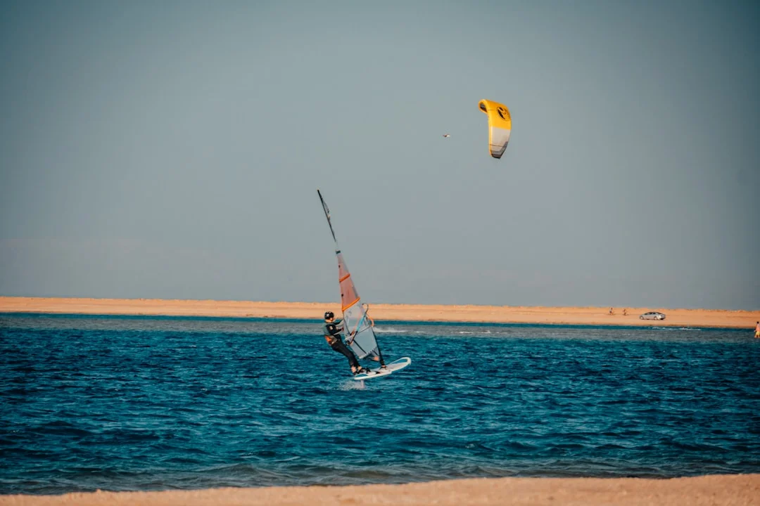 Multiple kitesurfers gliding across the flat, turquoise water of a Soma Bay lagoon, with mountains in the distance.