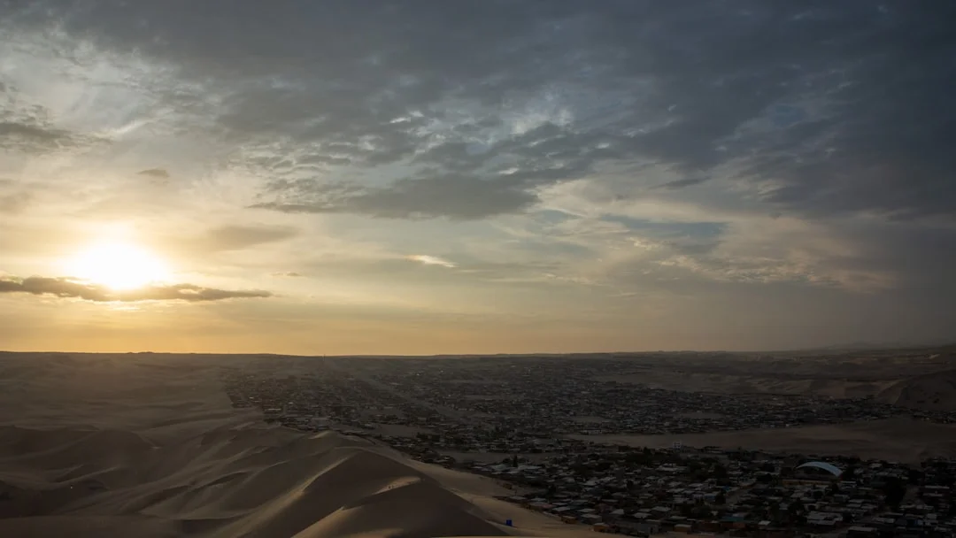 Vue aérienne du coucher de soleil glissant sur les dunes près de Dahab, sous un ciel rose-orangé.